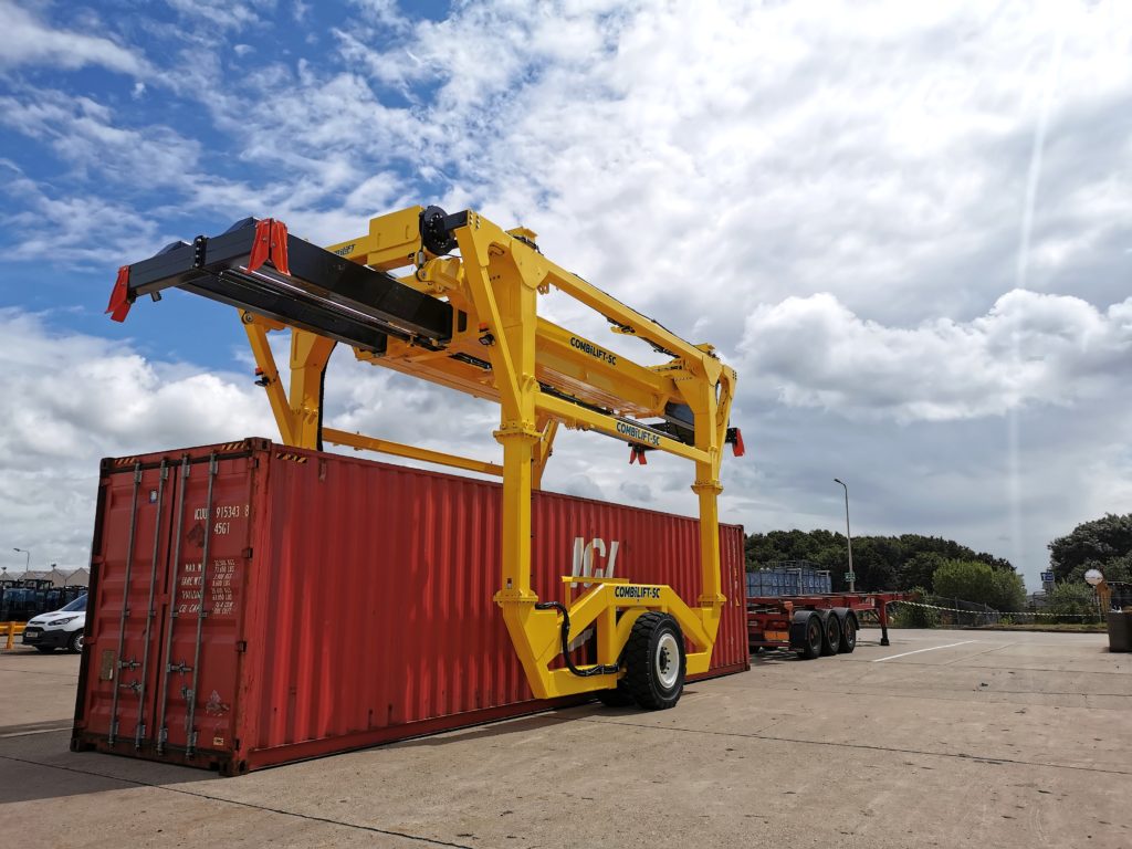 Yellow Combilift Straddle Carrier ready to lift red storage container