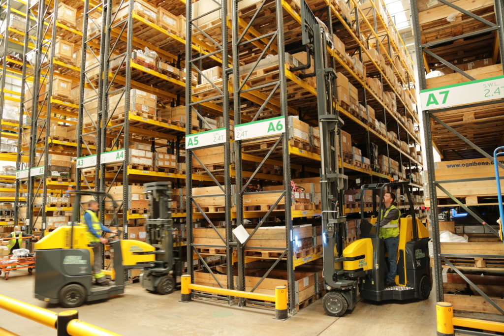 Two workers using two Aisle Master Order Pickers in a warehouse with stacks of pallettes